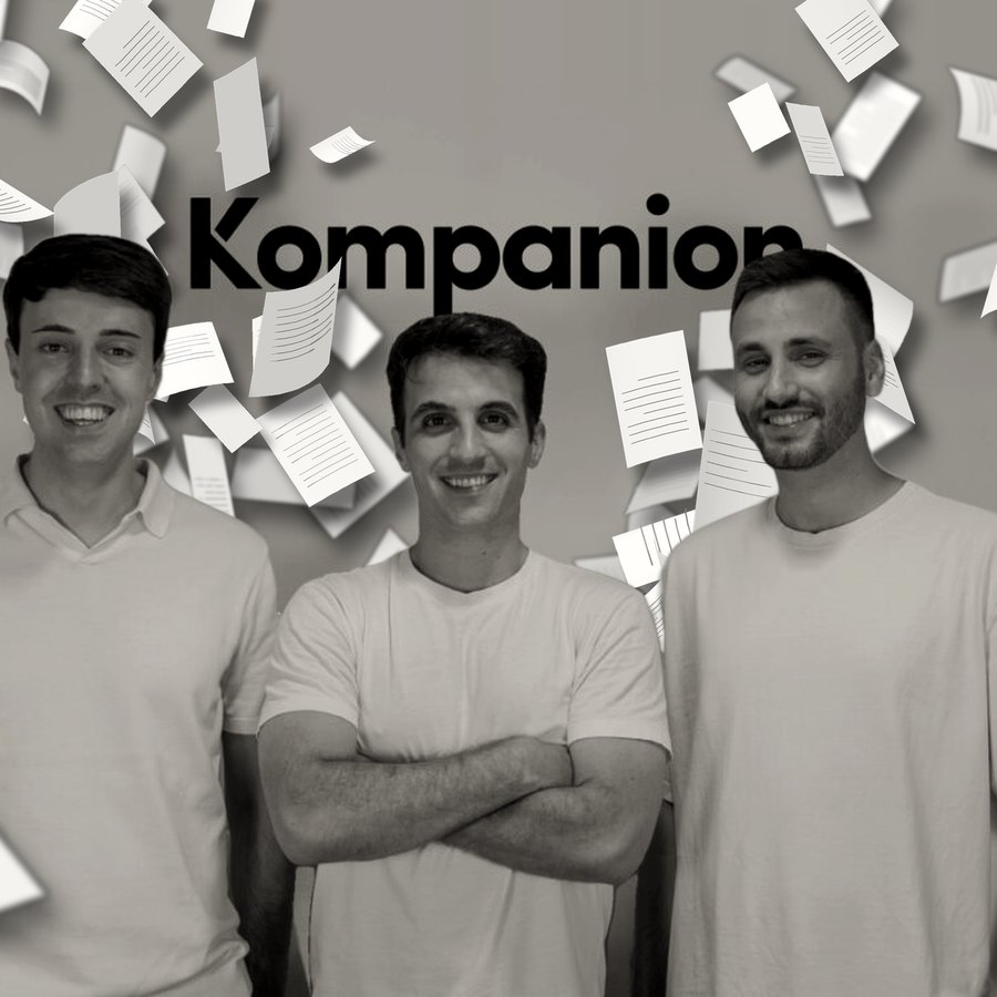 Los tres fundadores de Kompanion ante la pared con el logo de la empresa, en blanco y negro, mientras decenas de folios salen volando de detrás de ellos.